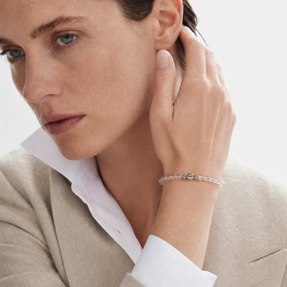 Clear Quartz 6mm Strand Bracelet worn on the wrist, showing clear round beads and the magnetic clasp with the hand beside the ear.