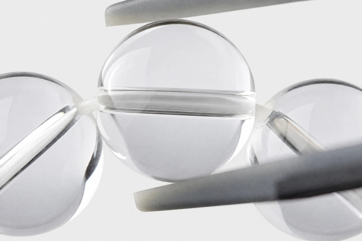Close-up of a clear quartz bead held between caliper jaws, showing the polished surface and wire through the drill hole.