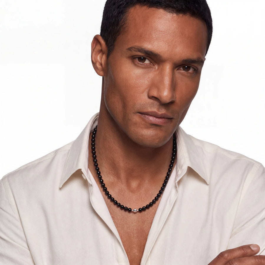 Black onyx bead necklace worn by a man in an open white shirt, angled portrait.