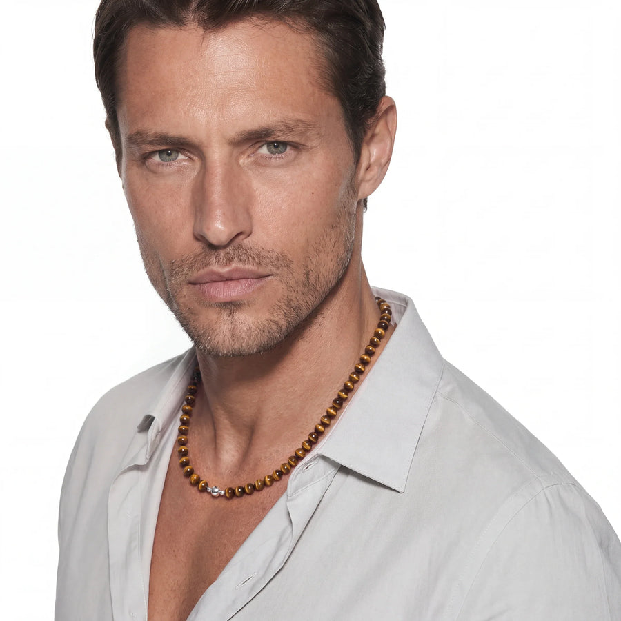 Close view of a golden tiger's eye bead necklace worn by a man in an open white shirt.