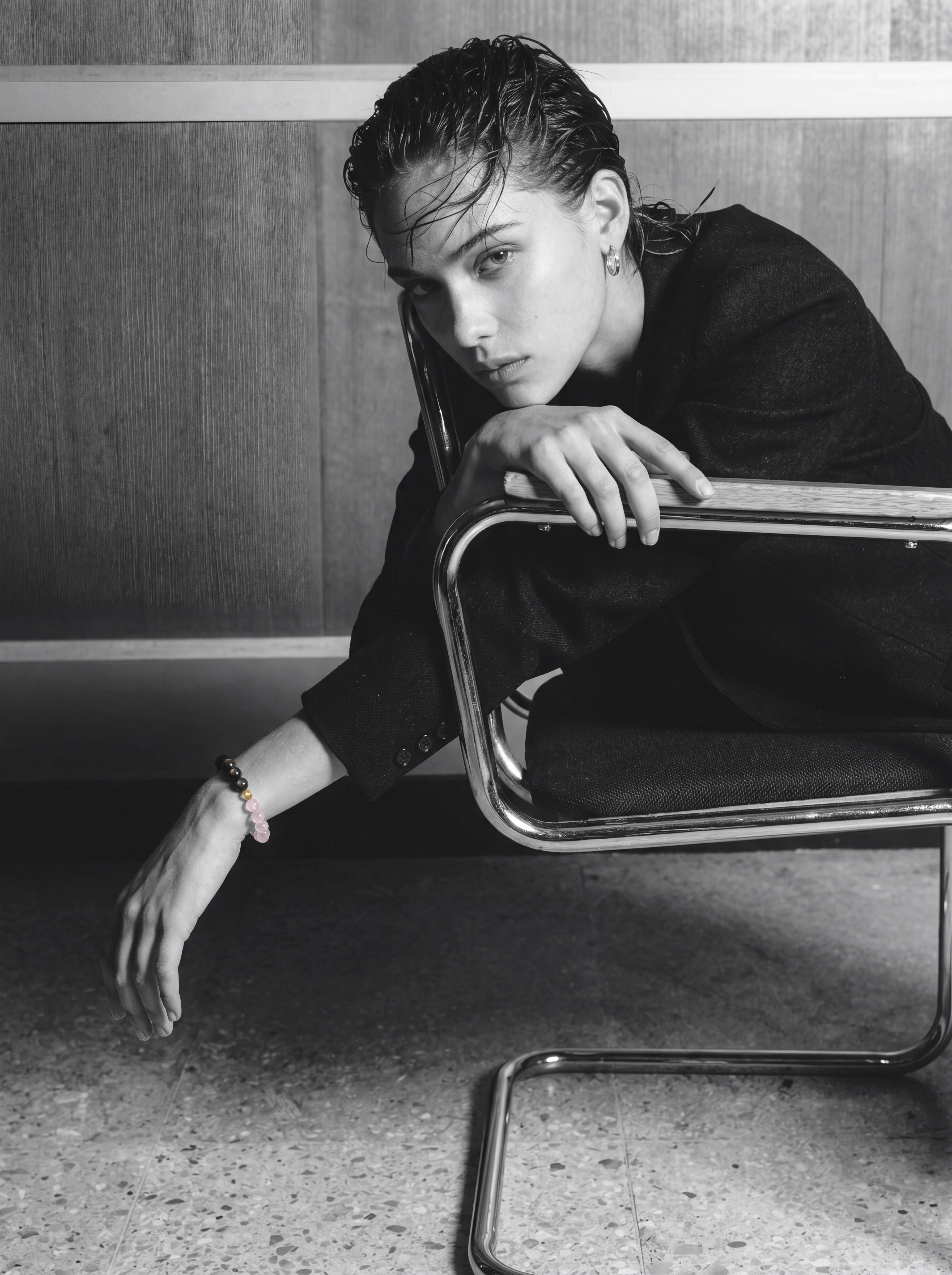 Person in dark clothing wearing a beaded bracelet beside a chrome chair