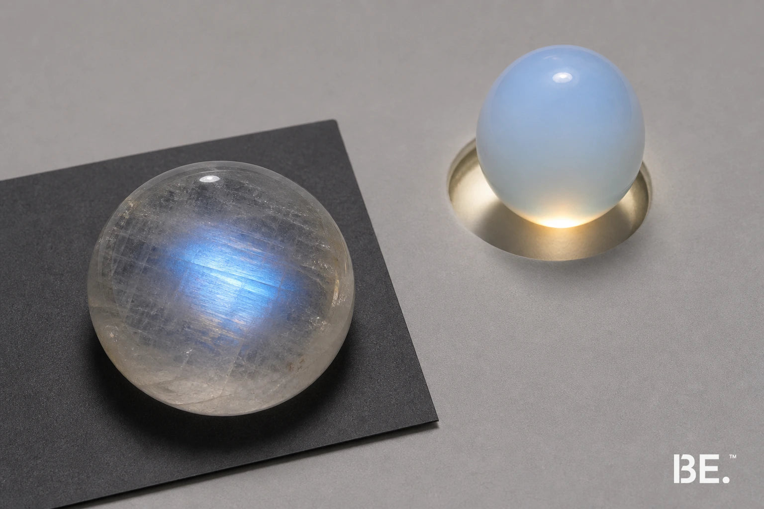 Moonstone with a localised blue adularescent band beside opalite-style glass with an even glow — BE.