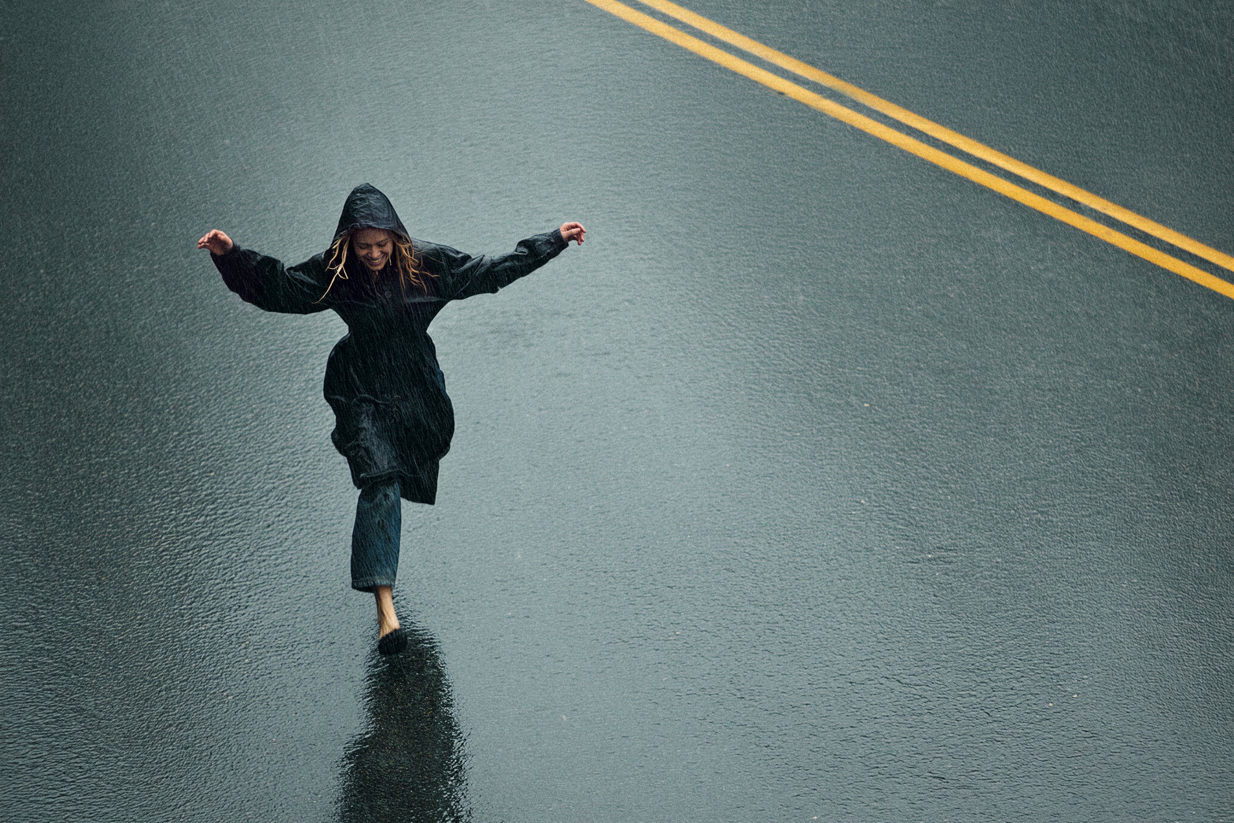 Person balancing on one foot on a rain-darkened road, viewed from above.