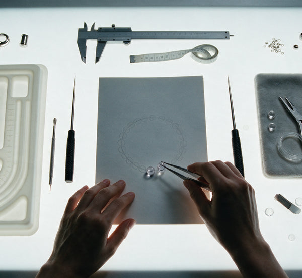 Hands assembling a clear quartz bracelet at an illuminated studio workbench