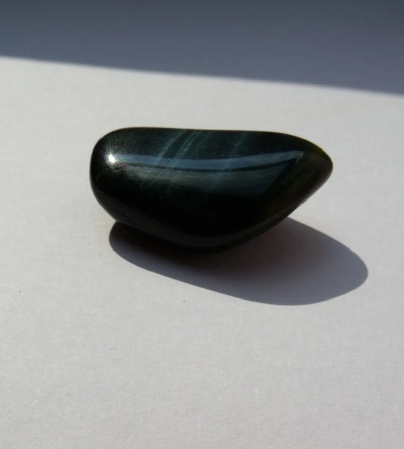 A polished blue-black hawk’s-eye stone with pale blue-grey streaks across its upper surface.