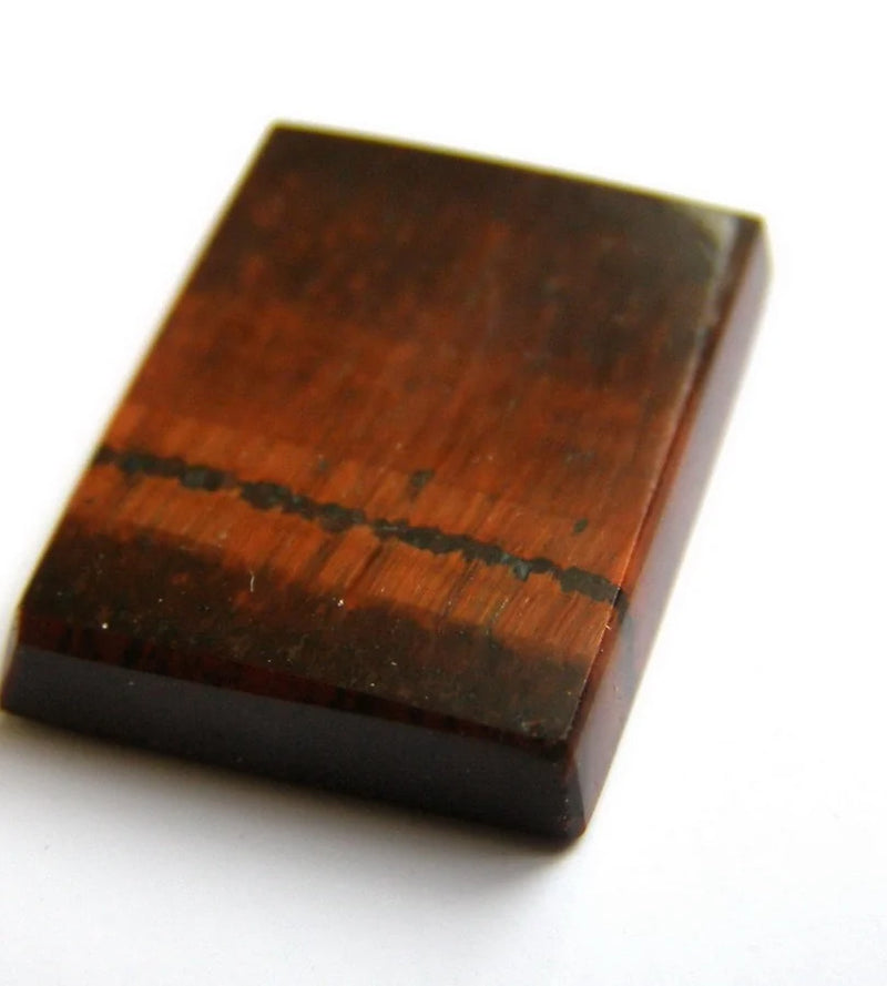 A polished rectangular red tiger’s-eye cabochon with fine parallel fibres and a dark line across its face.