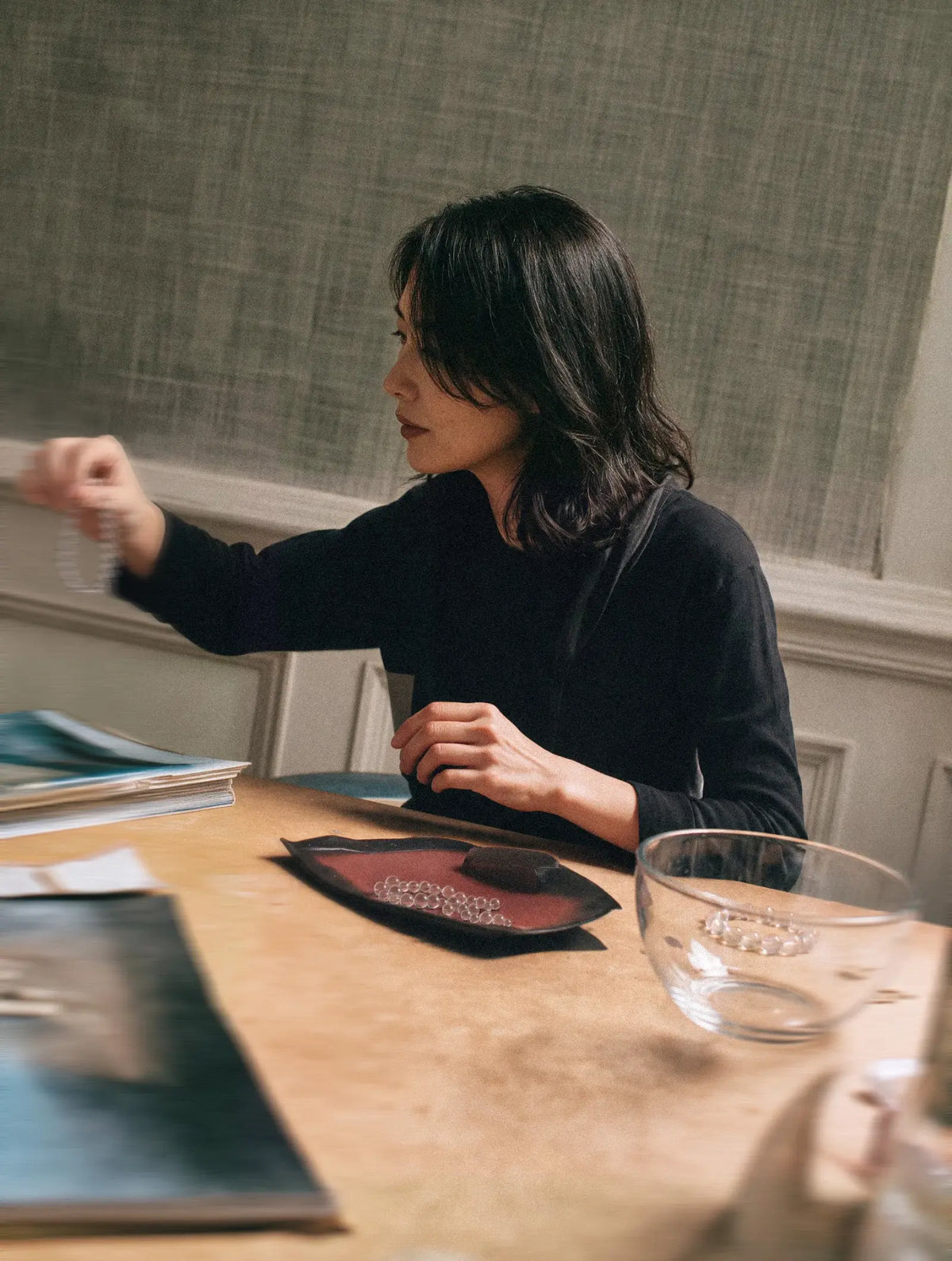 Woman seated at a studio worktable with materials and open reference books.