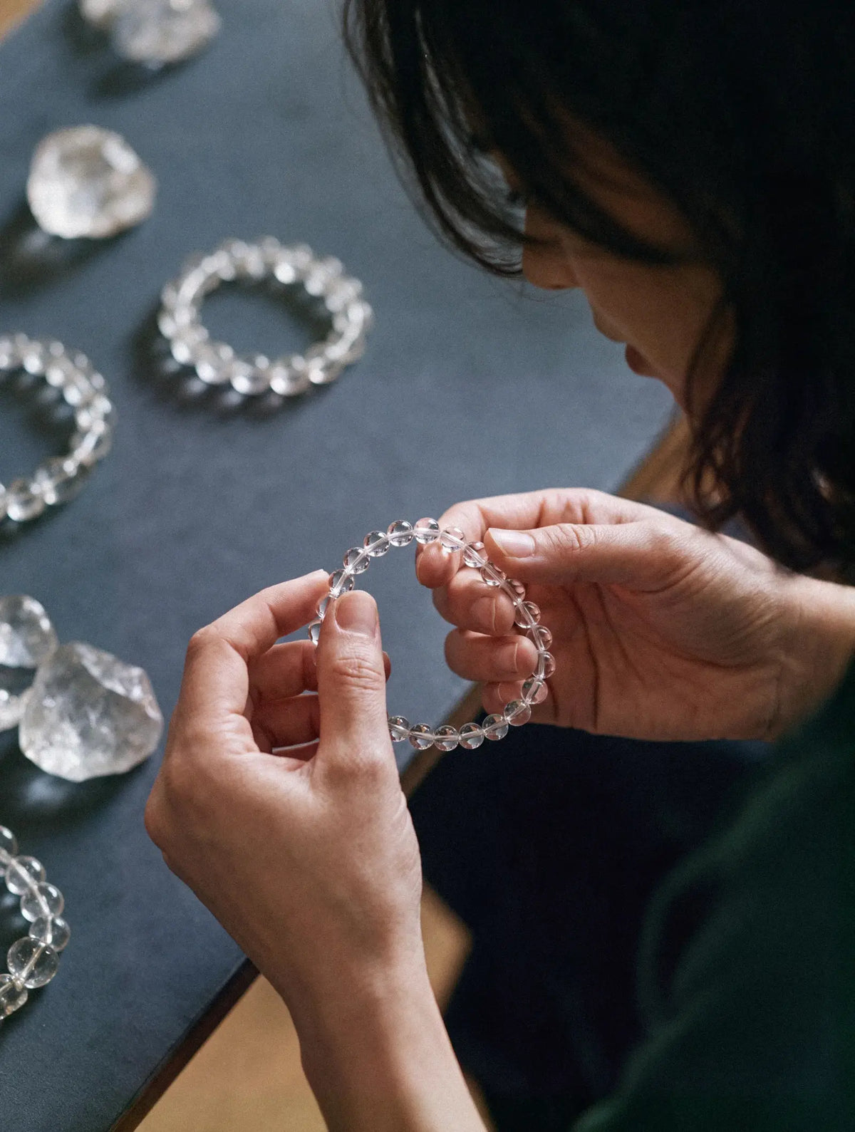 Hands examining a transparent bead strand above a dark worktable.