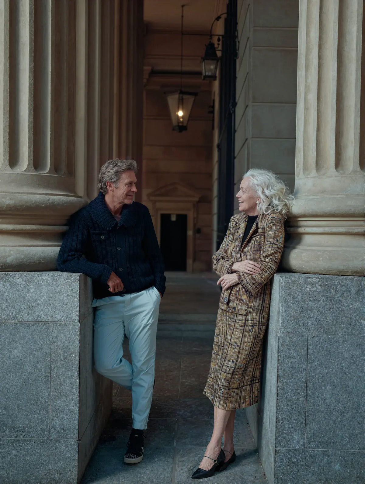Two people in conversation outside a stone-columned building.