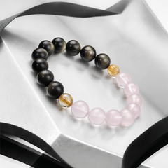 The Obsidian, Pink Quartz and Rutilated Quartz Bracelet on a reflective white surface, BE.