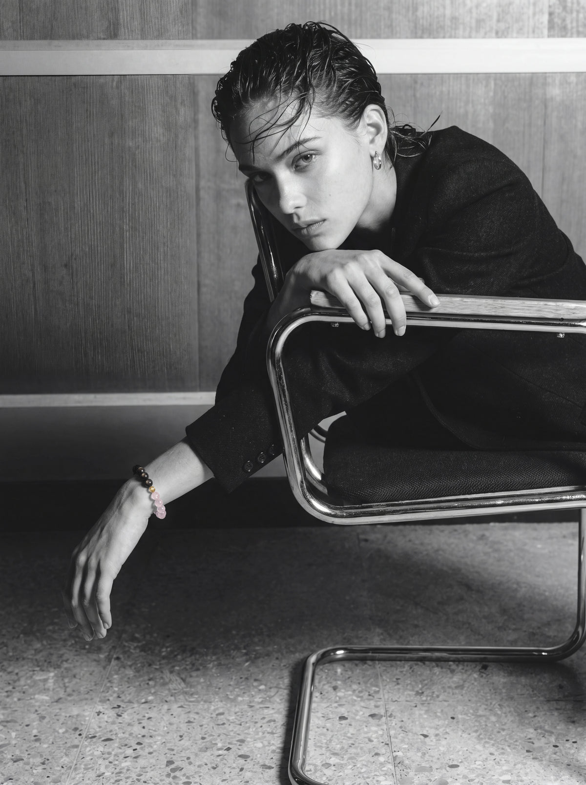 Person in dark clothing wearing a beaded bracelet beside a chrome chair