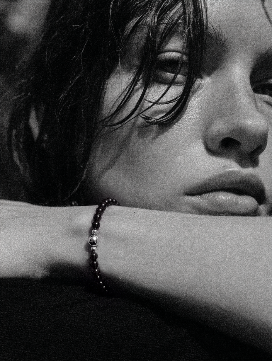 Close-up of a woman resting her face above an arm wearing a dark bead strand.