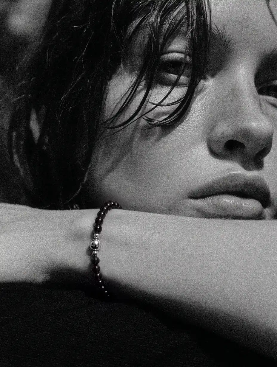Close-up of a woman resting her face above an arm wearing a dark bead strand.