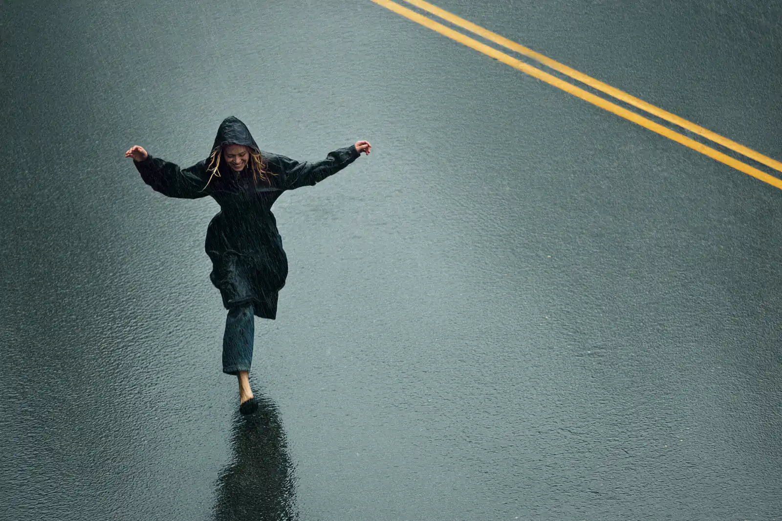 Person balancing on one foot on a rain-darkened road, viewed from above.